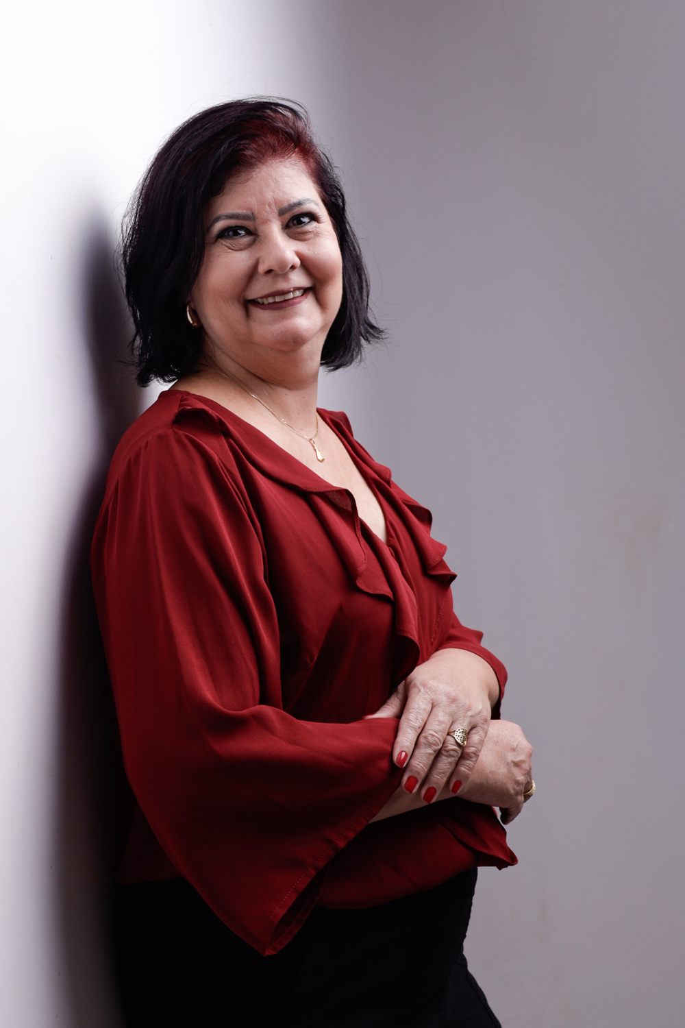 Eliane Rossato de blusa vermelha, sorrindo, encostada em uma parede clara